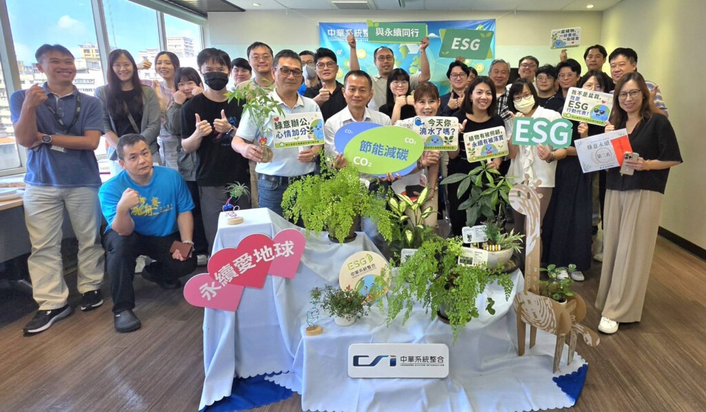 Group of colleagues at an ESG event posing with signs about carbon reduction, surrounded by plants in a showroom-like space.
