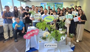 Group of colleagues at an ESG event posing with signs about carbon reduction, surrounded by plants in a showroom-like space.